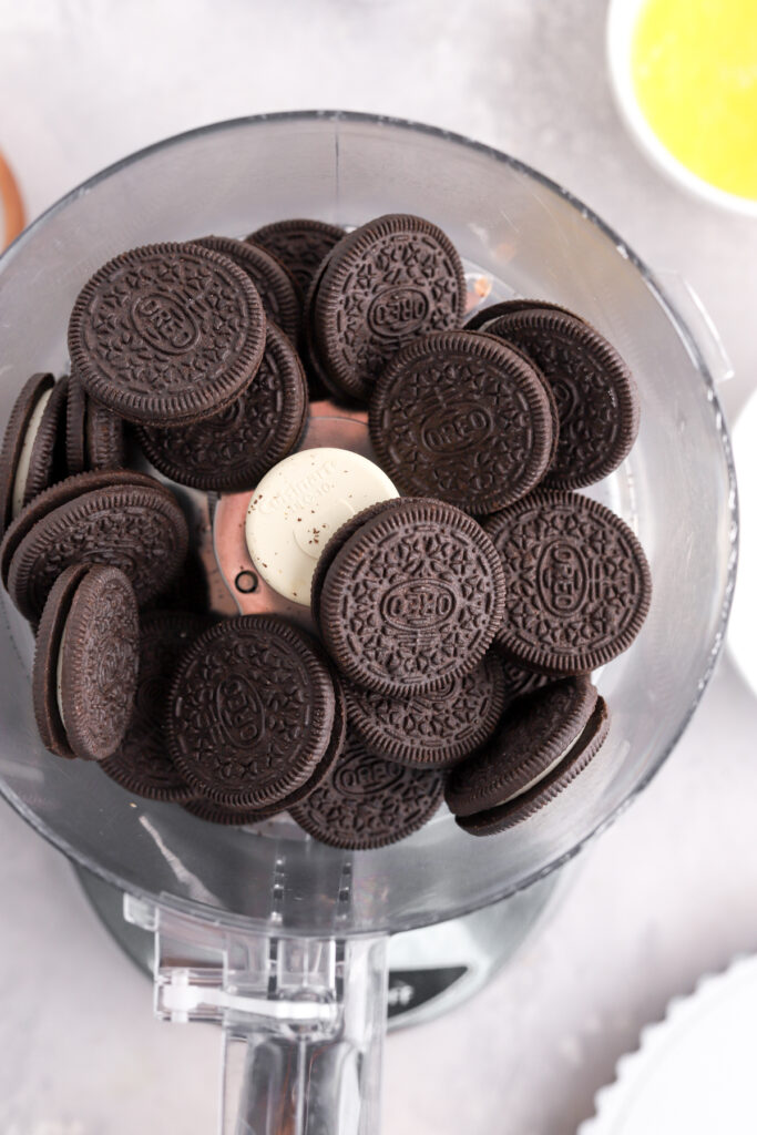 Oreo cookies in a food processor and a bowl of melted butter.