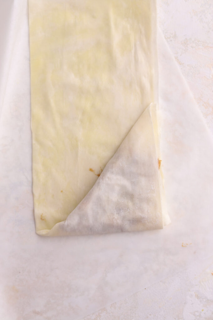 Strips of phyllo dough being folded in a triangle with a filling inside.