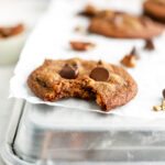 A chocolate chip cookie with a bite in it on a baking sheet.