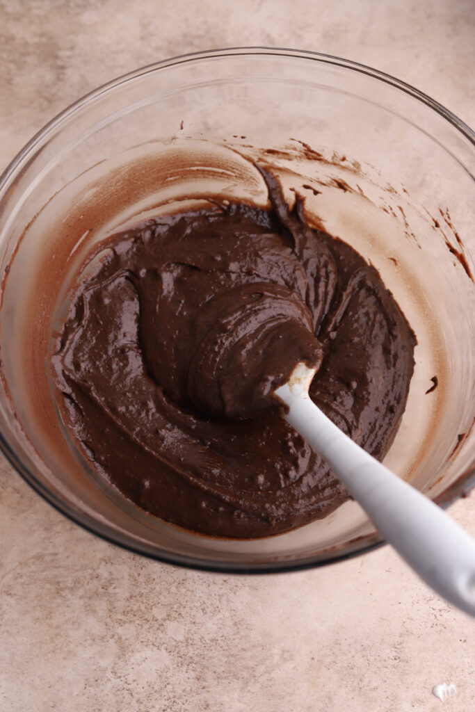 A glass mixing bowl with chocolate batter and a spatula. 