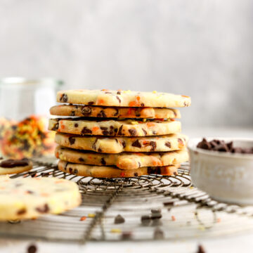 A stack of sprinkle and chocolate chip filled cookies on a rack.