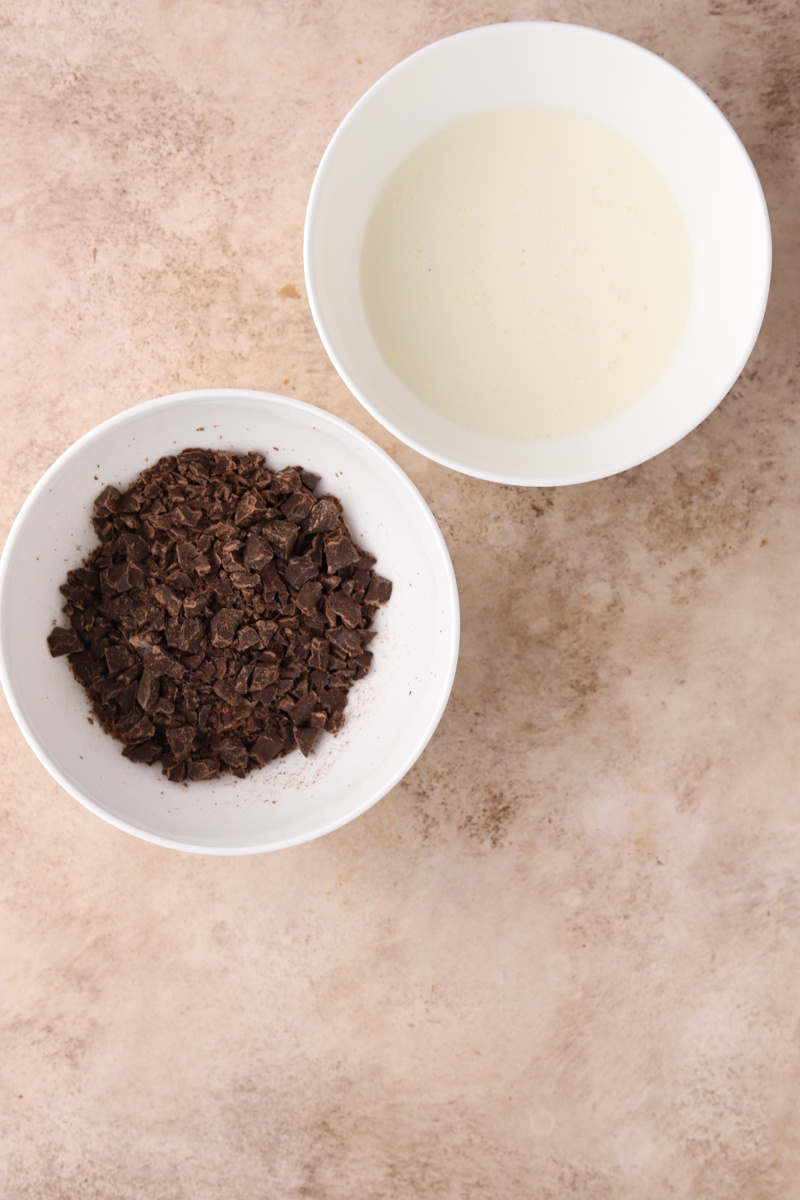 A white bowl with chopped chocolate and a white bowl with heavy cream.