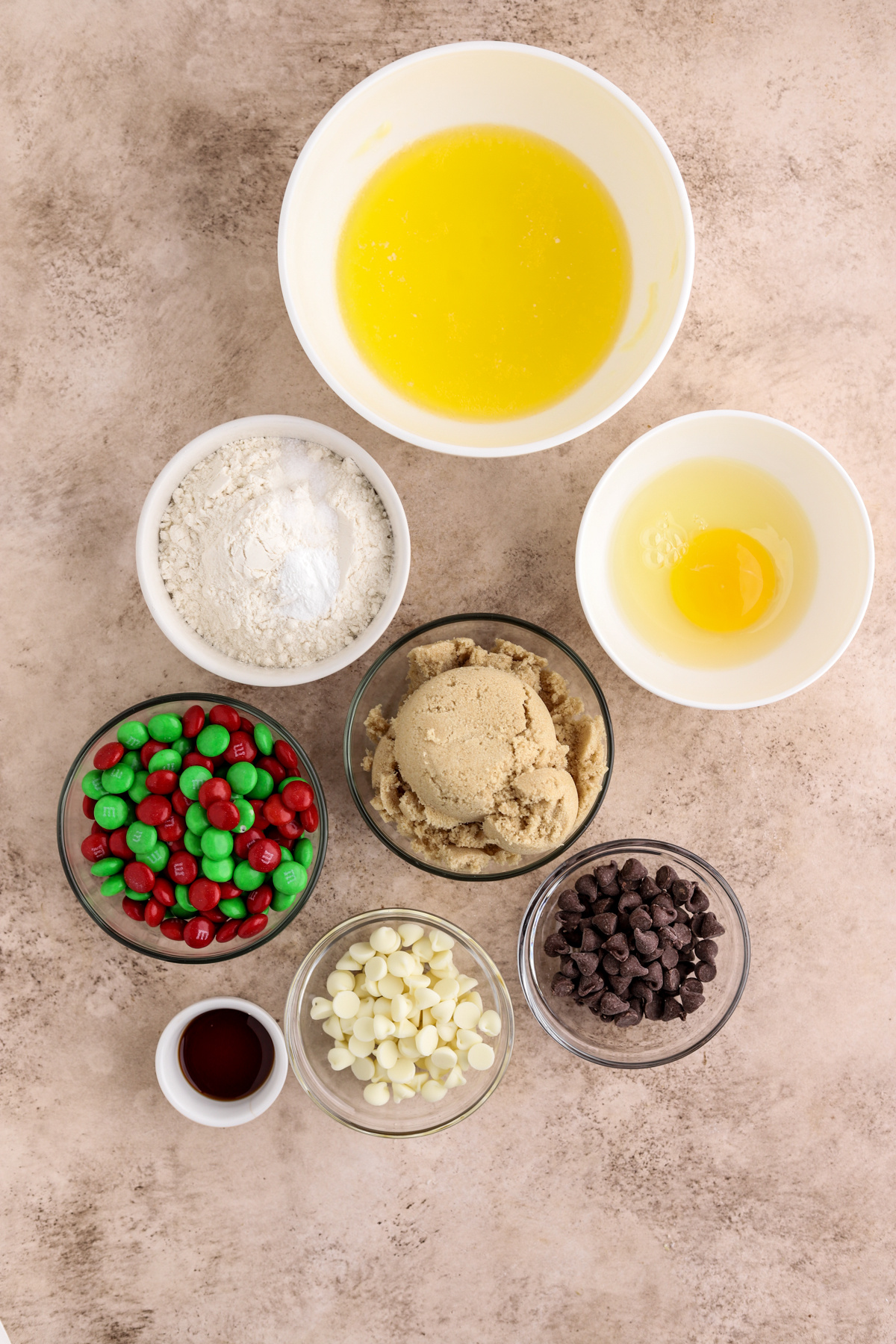 Small white and glass bowls filled with melted butter, an egg, sugar, flour and M&Ms. 