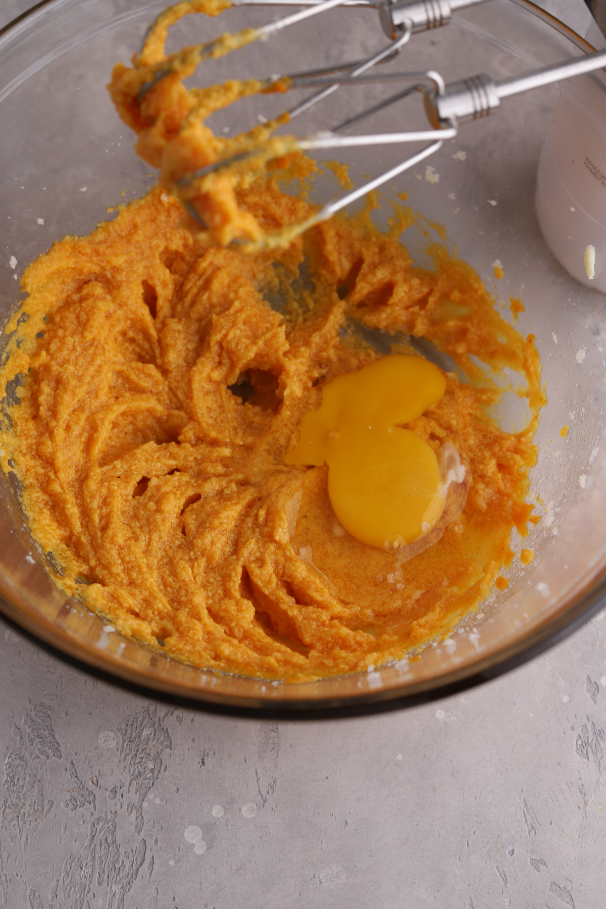 Orange pumpkin cookie dough and an egg on top in a glass bowl.