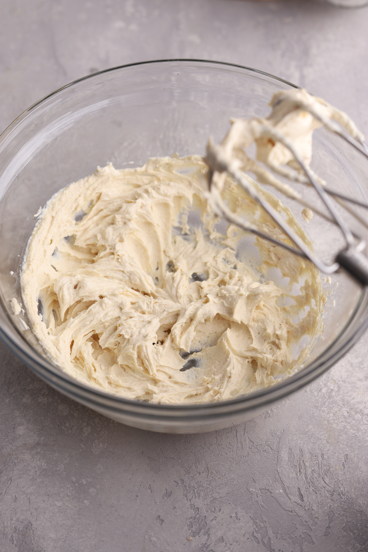 Cream cheese icing in a glass mixing bowl with a mixer. 