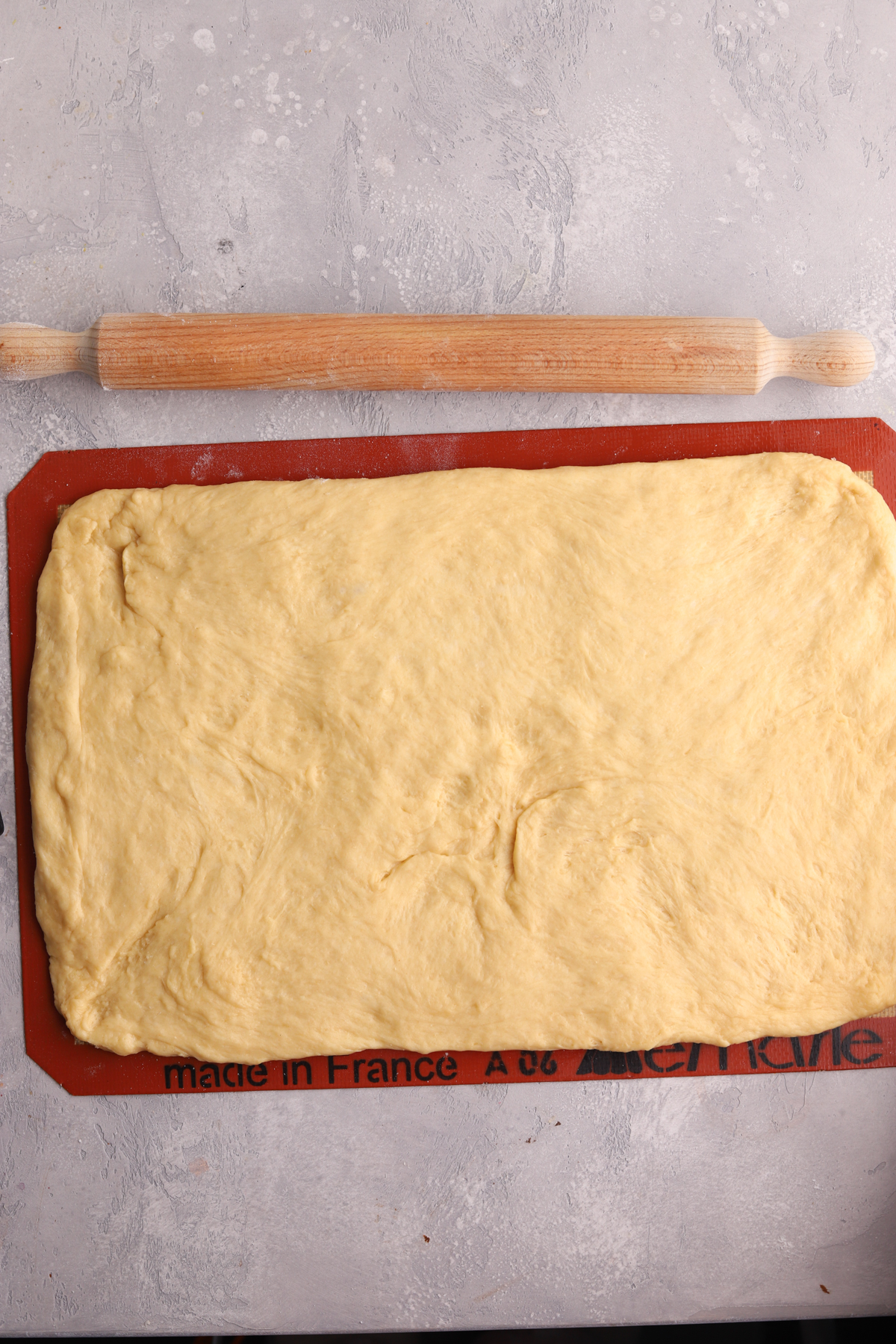 Cinnamon roll dough rolled in a rectangle and a rolling pin.