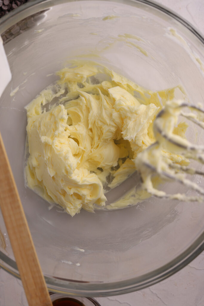 Creamed butter in a glass bowl with a mixer and spatula.