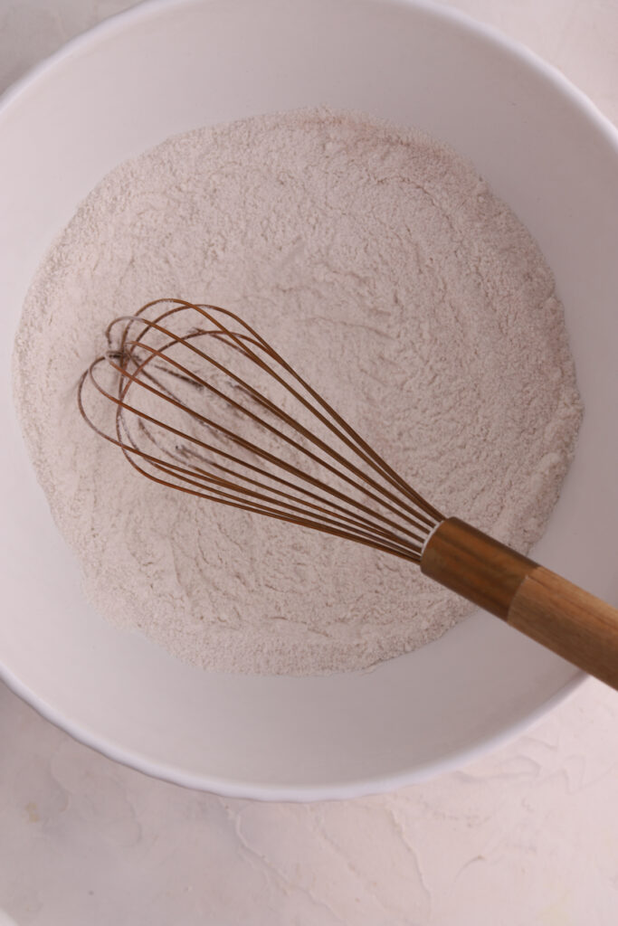 A white mixing bowl with dry ingredients and a whisk. 