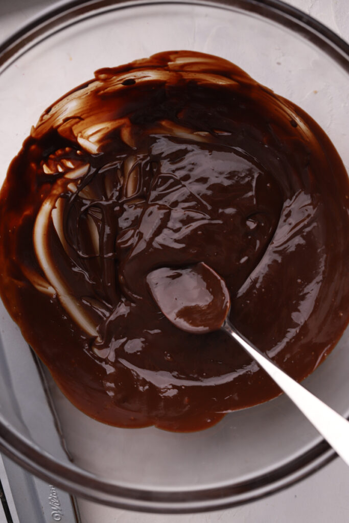 Chocolate ganache in a glass bowl with a spoon. 