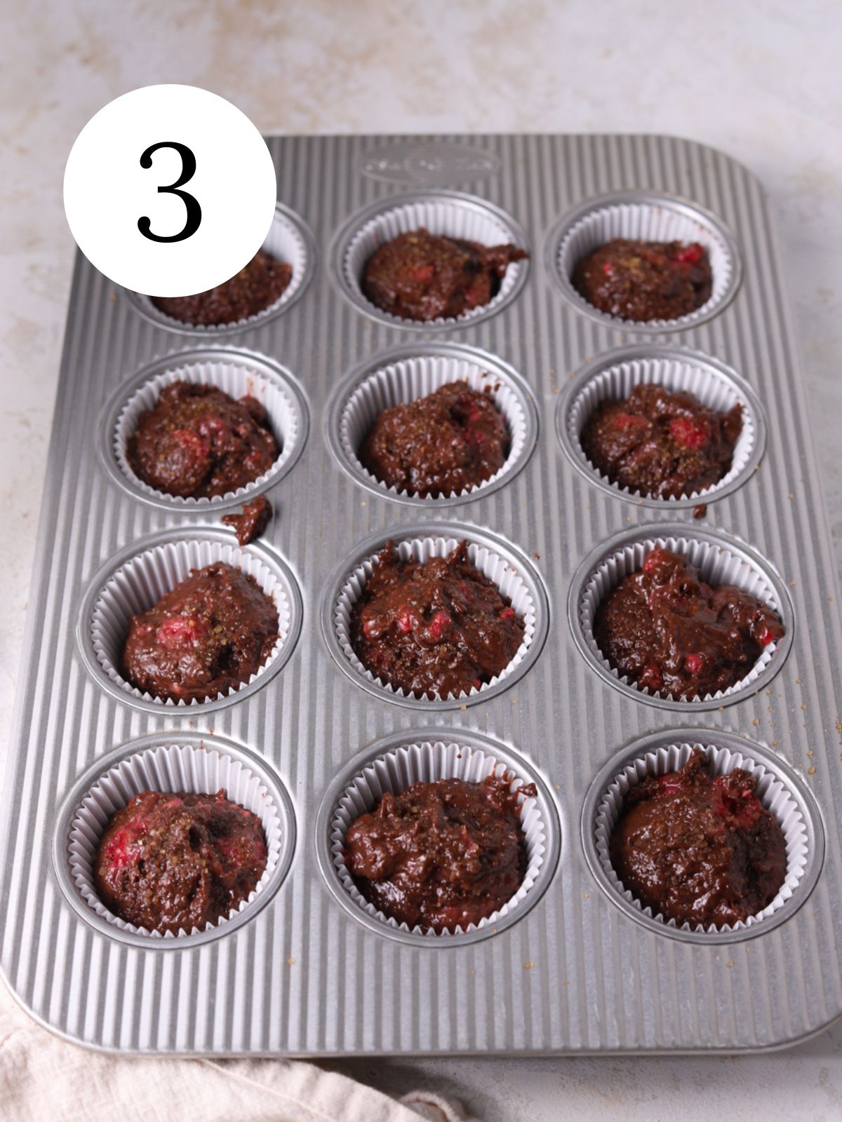 A muffin pan with chocolate raspberry muffin batter in some of the muffin cavities.