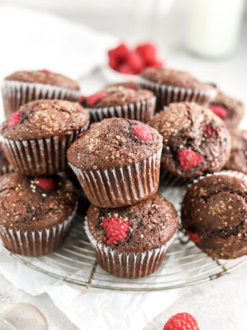 A batch of chocolate muffins with raspberries on a rack.