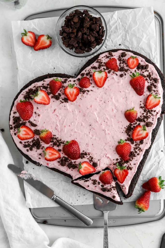 A heart shape chocolate cake decorated with strawberry frosting, fresh strawberries and chocolate crumbles. 