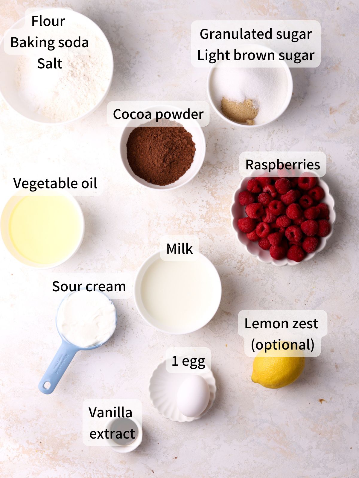 Labeled ingredients needed to make raspberry muffins laid out on a table.