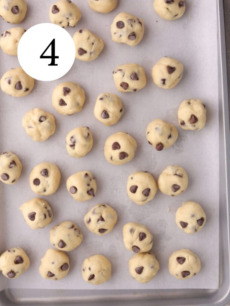 Chocolate chip cookie dough balls on a baking sheet with parchment paper.