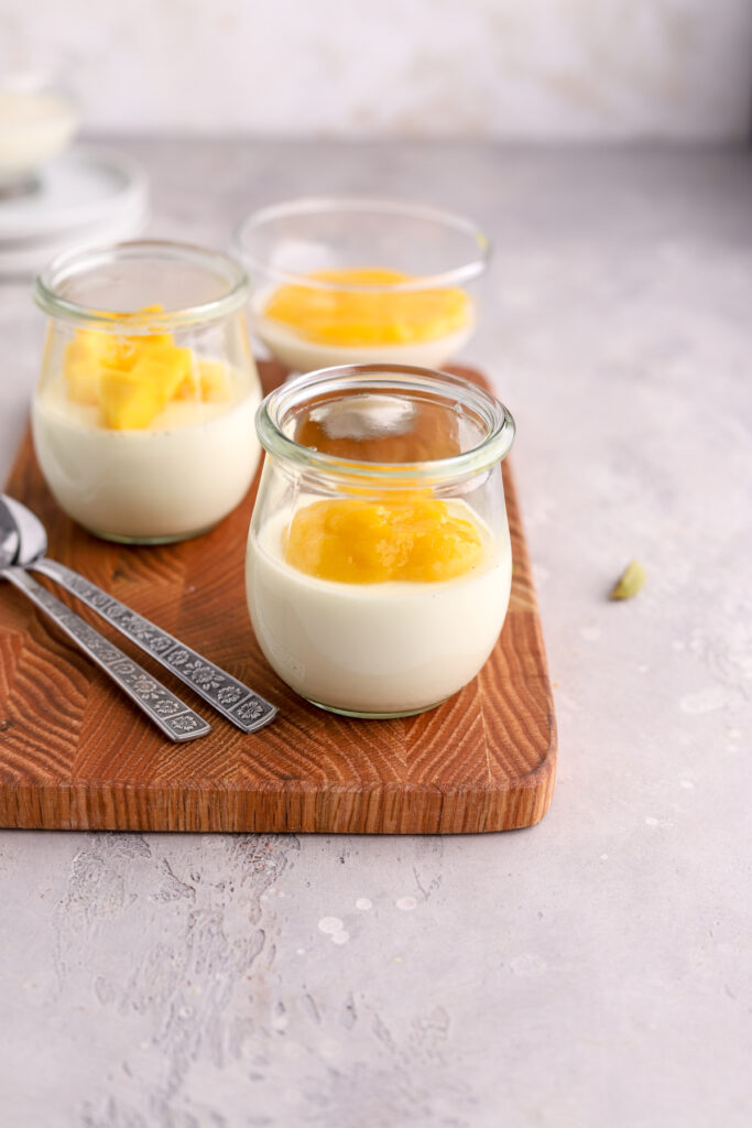Glass jars with panna cotta topped with mango coulis and fresh chopped mango. 