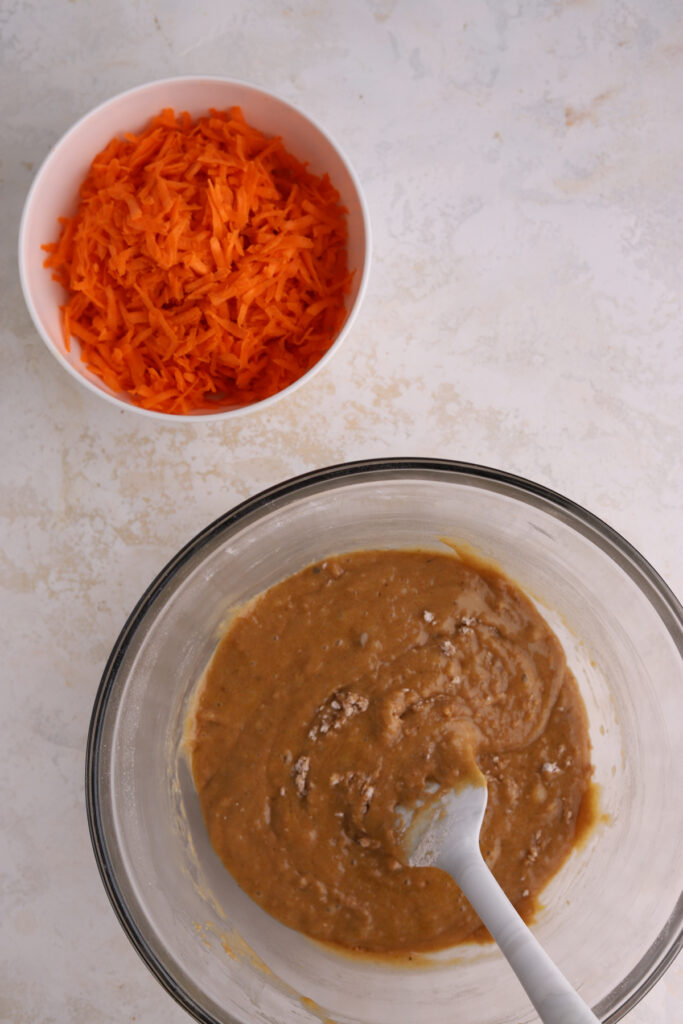 Carrot cake batter in a mixing bowl and a bowl of grated carrots. 