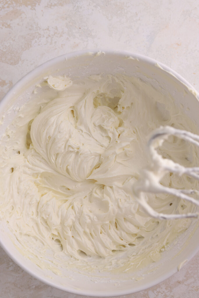 Cream cheese frosting in a white bowl with a mixer. 