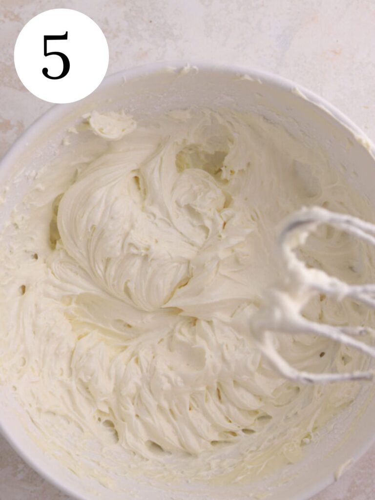 Cream cheese frosting in a white bowl with a mixer. 