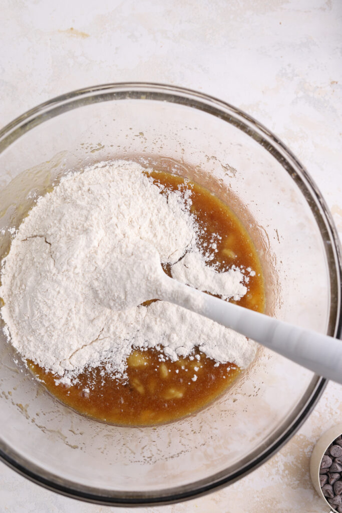 Flour being stirred into banana batter in a bowl. 
