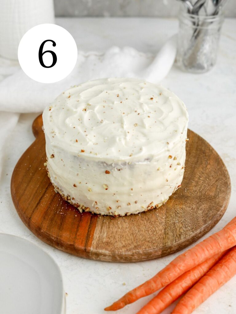 A frosted mini carrot cake on a platter next to some carrots. 