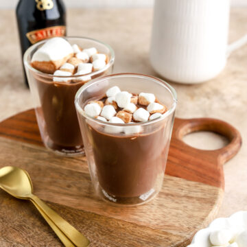 Two glasses of hot chocolate topped with marshmallows and a bottle of Baileys.