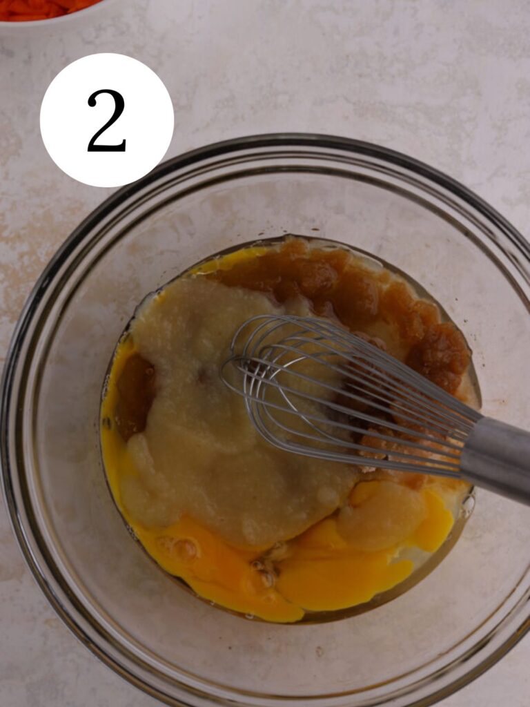 A glass bowl with wet ingredients being whisked together.