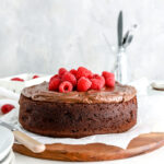 Chocolate cake with chocolate frosting and raspberries on a wooden platter.