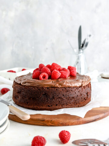 Chocolate cake with chocolate frosting and raspberries on a wooden platter.