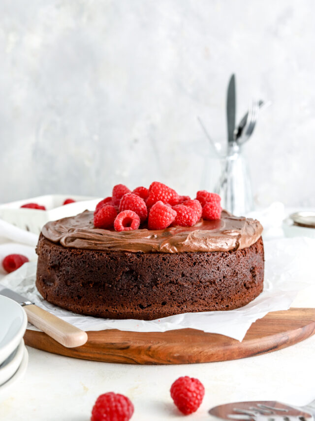 Chocolate cake with chocolate frosting and raspberries on a wooden platter.