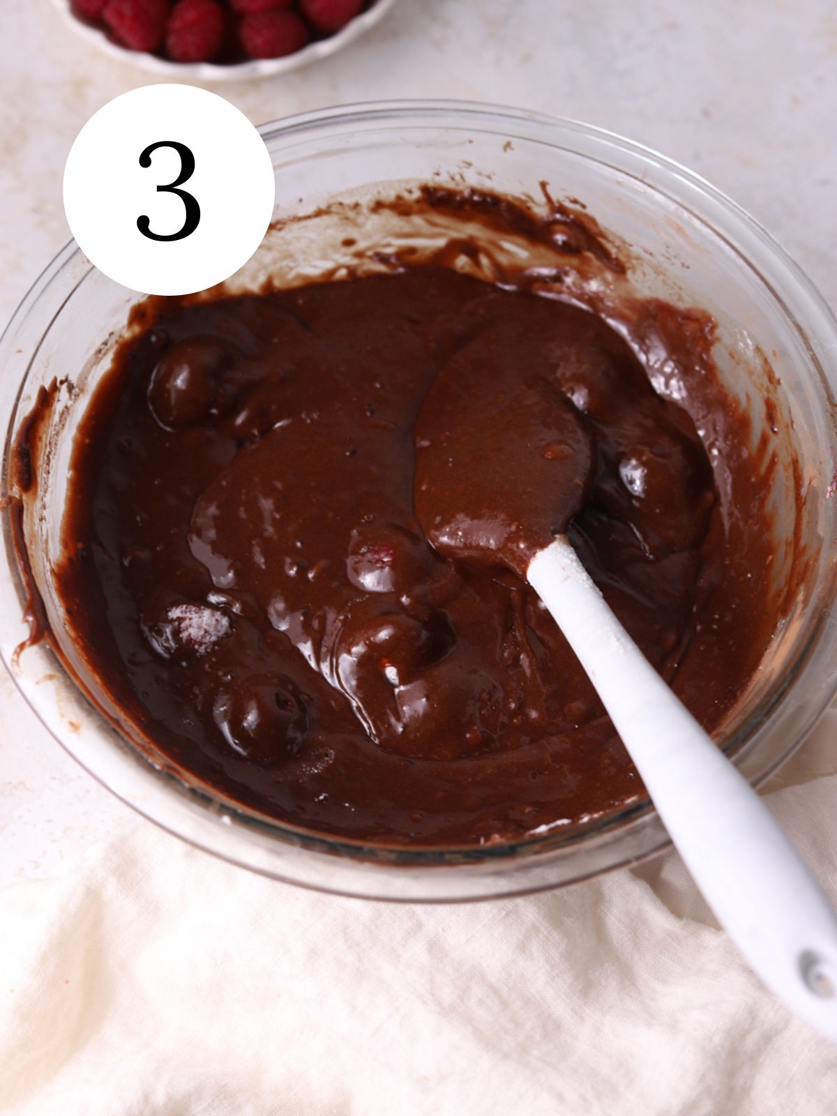 Raspberries stirred into chocolate cake batter with a spatula.