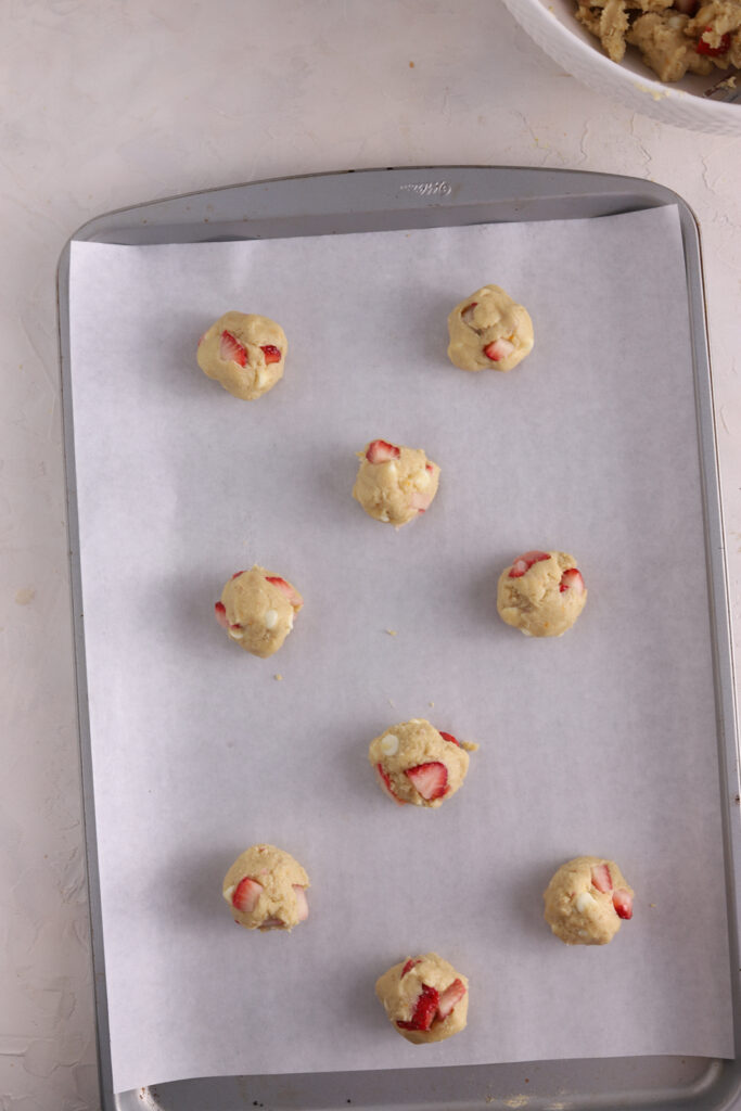 Strawberry cookie dough rolled into balls on a baking sheet.