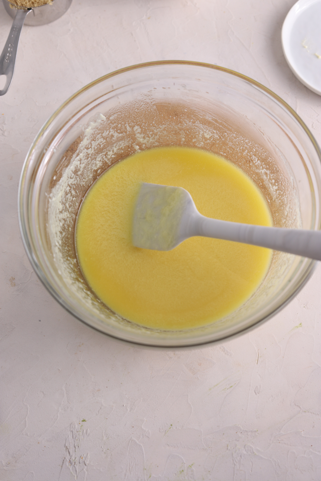 A glass mixing bowl with melted butter and a spatula. 