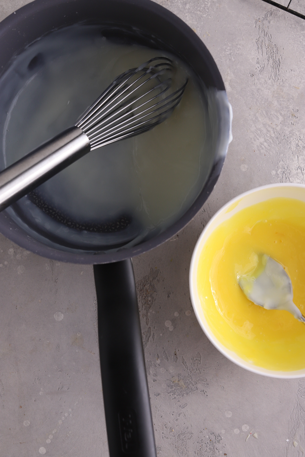 A saucepan with a whisk in it and a white bowl with egg yolks. 