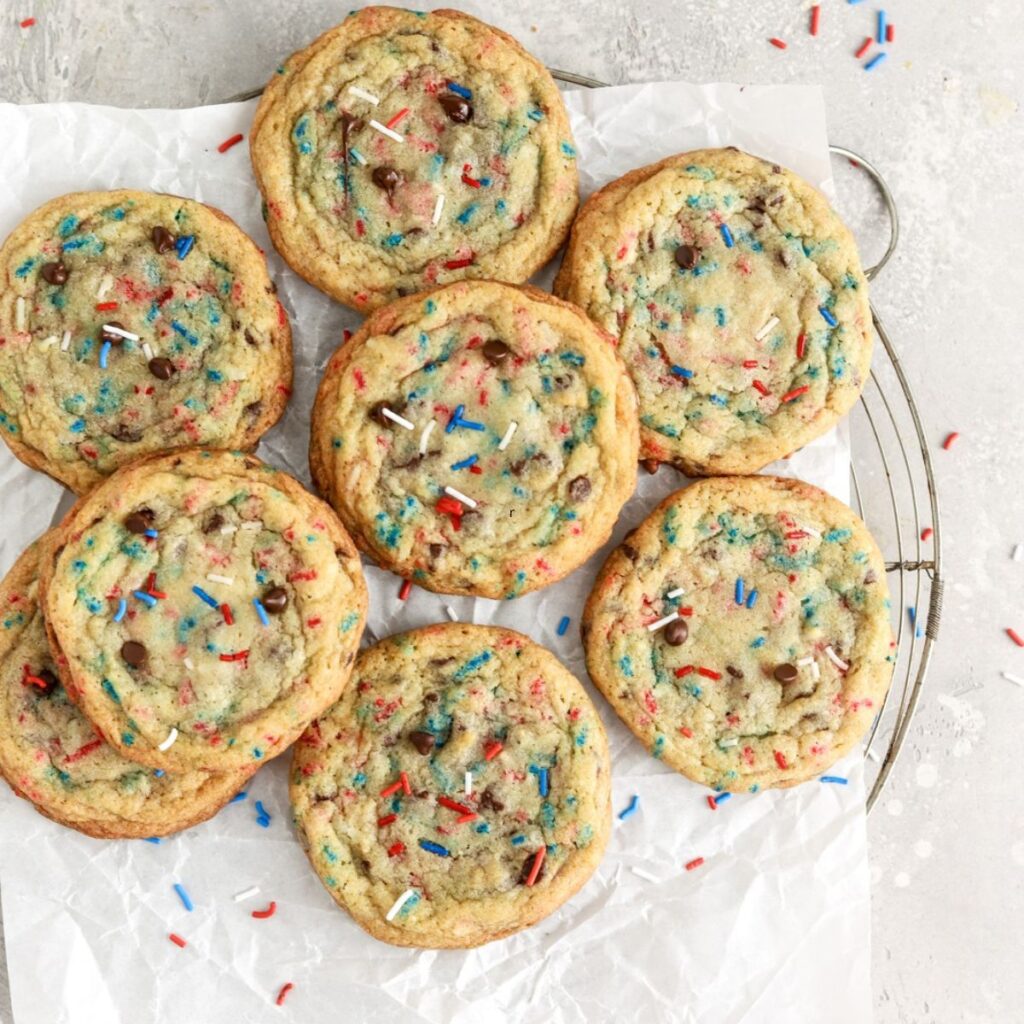 A batch of cookies with chocoolate chips and sprinkles on a rack.
