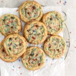 A batch of cookies with chocoolate chips and sprinkles on a rack.