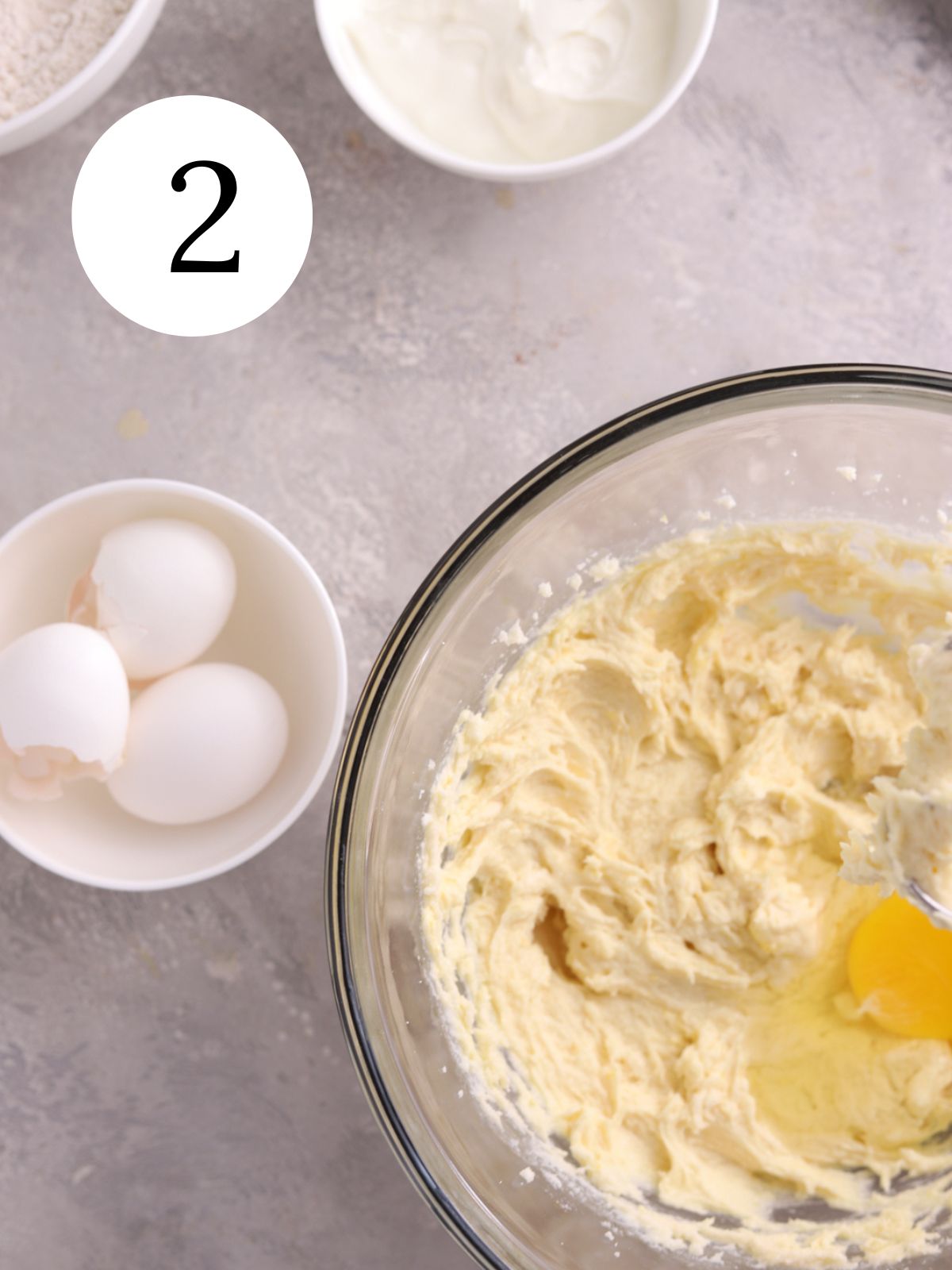 Eggs being added to a bowl of cake batter and a bowl of yogurt.