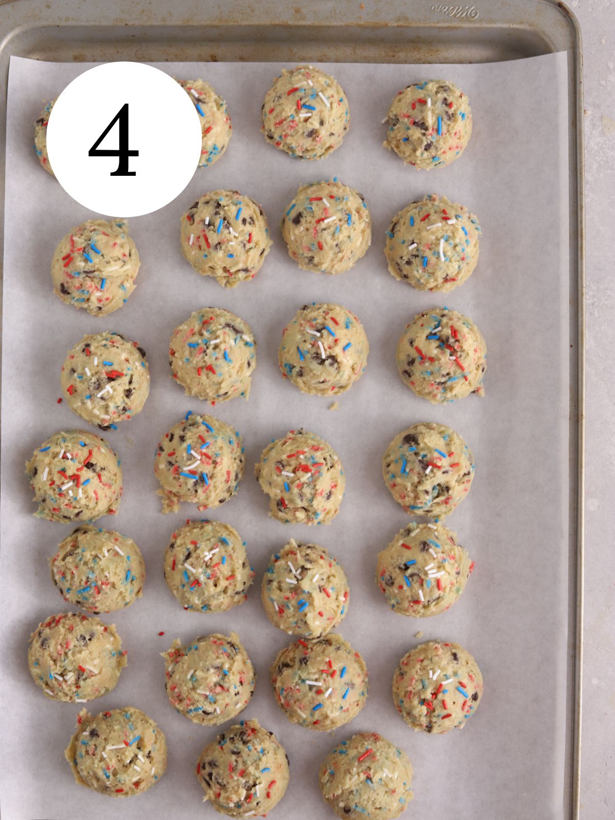A baking sheet lined with parchment paper with a batch of Fourth of July sprinkle cookie dough balls.