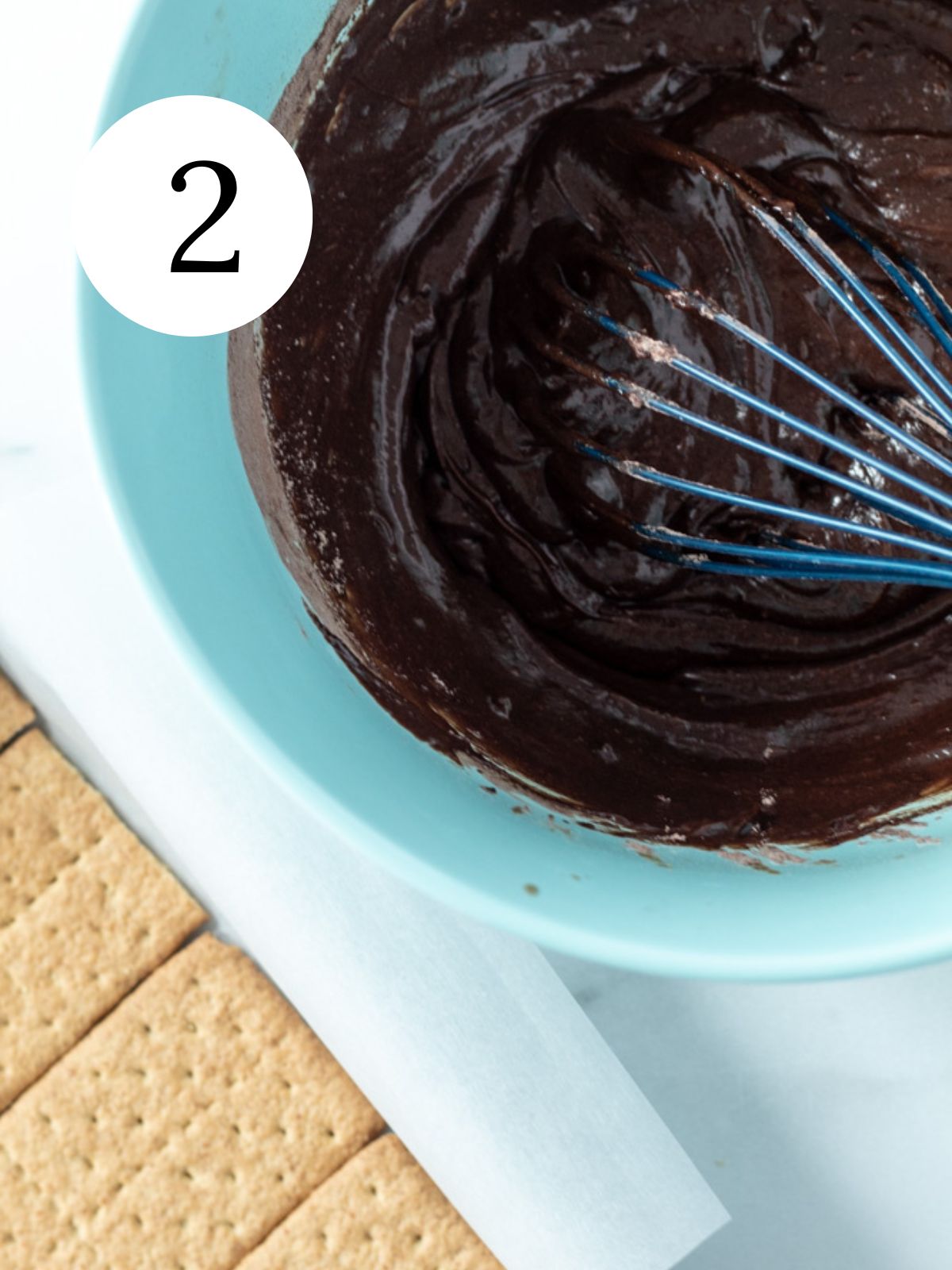 Brownie batter in a bowl with a whisk in it and graham crackers in a pan. 