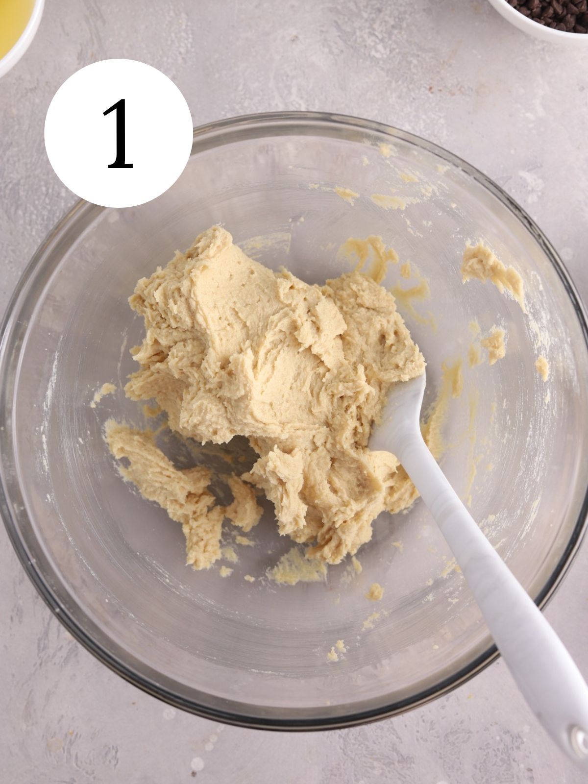 A glass mixing bowl with creamed butter and sugar and a spatula.