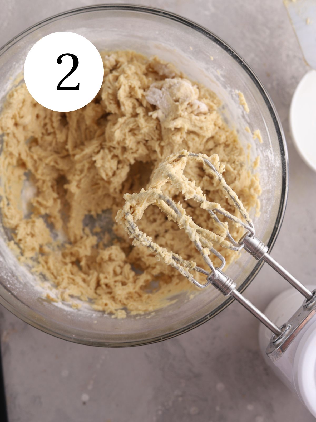 A glass bowl with cookie dough and a mixer next to it.