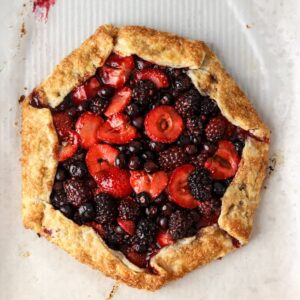 A golden brown galette filled with mixed berries on parchment paper.