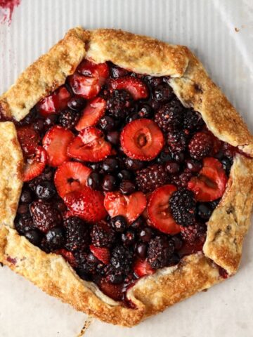 A golden brown galette filled with mixed berries on parchment paper.