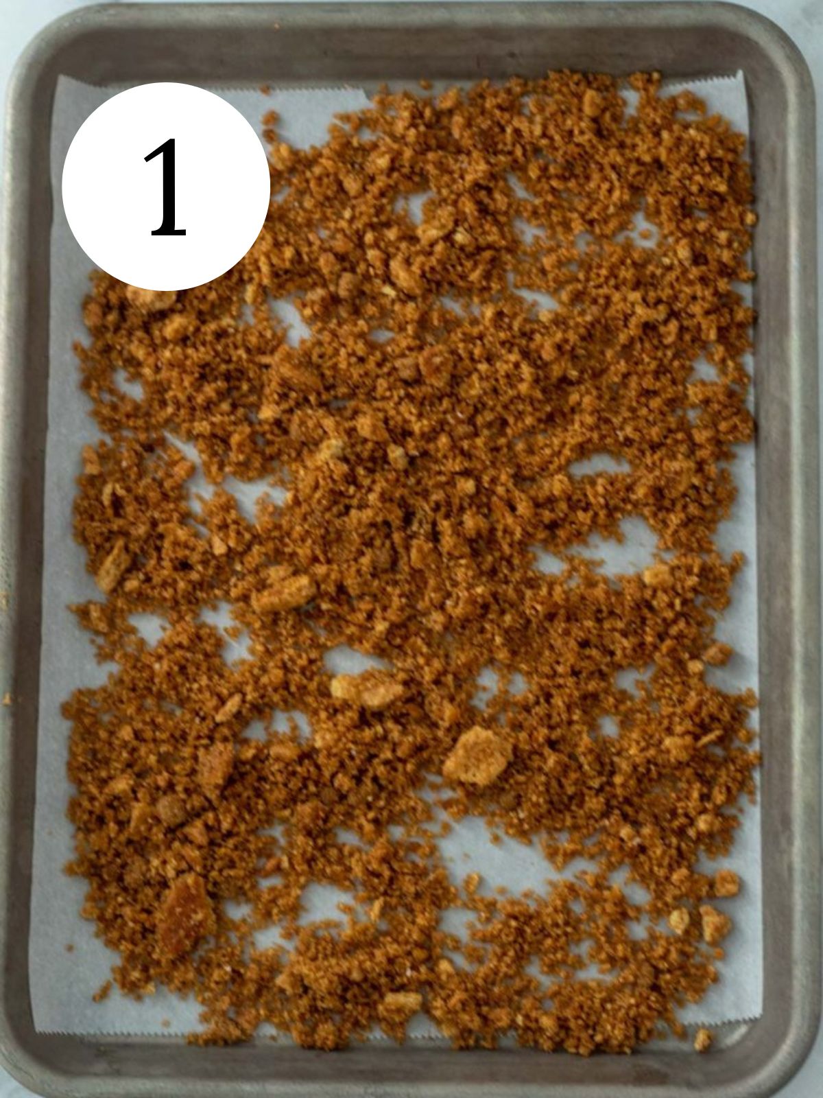 Toasted graham cracker crumbs on a baking sheet lined with parchment paper. 