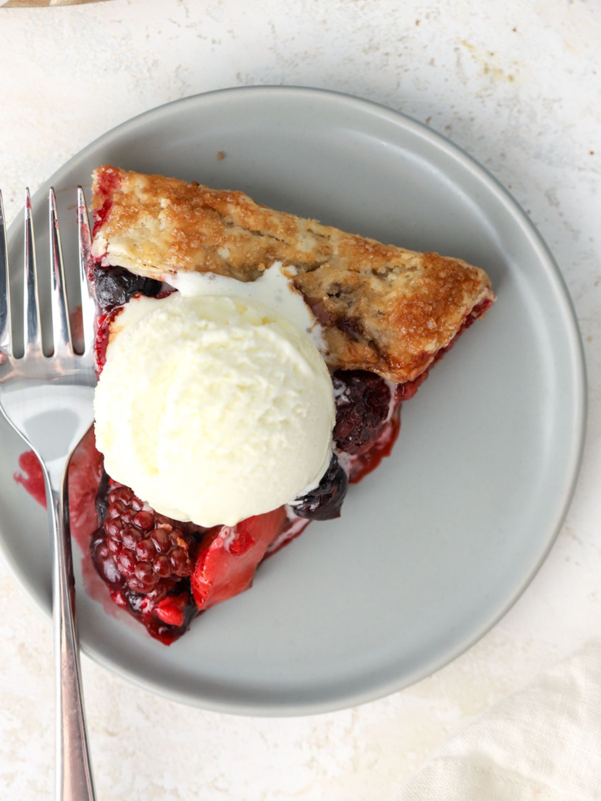 A slice of berry galette on a plate with ice cream on top. 