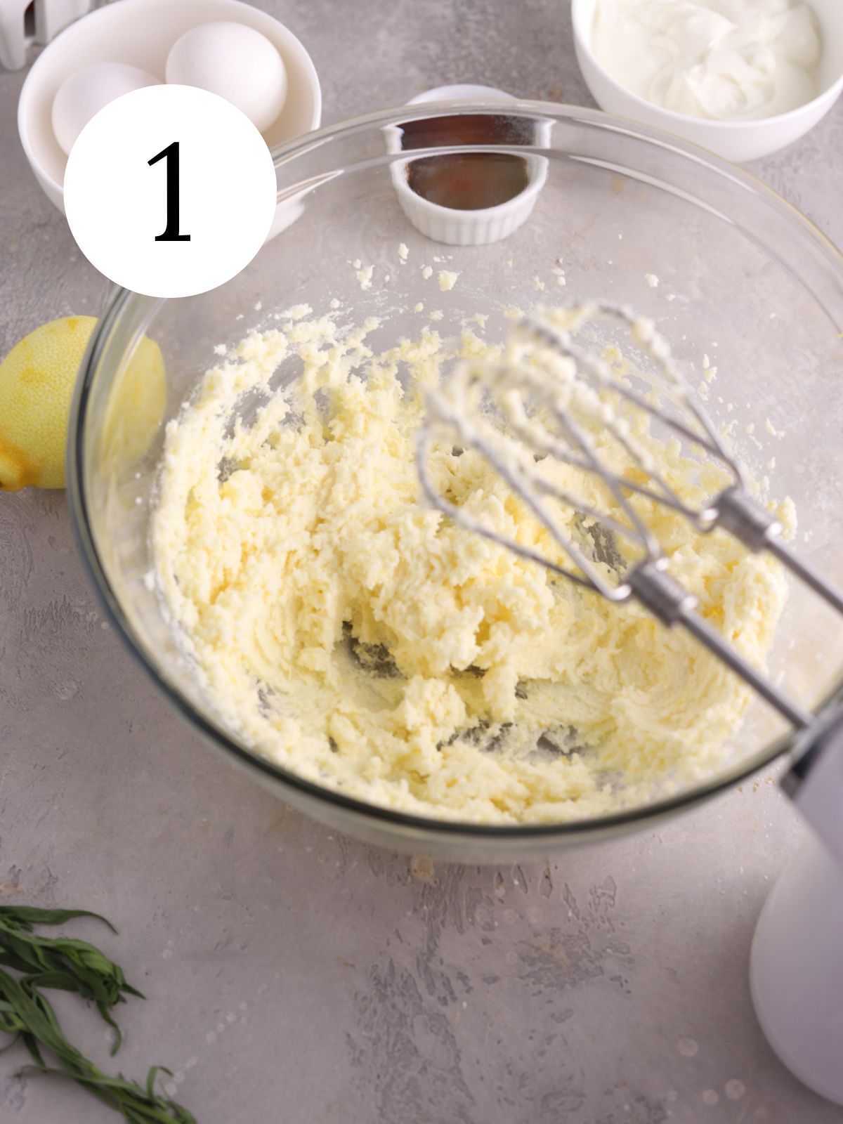 A glass mixing bowl with creamed butter and sugar next to an electric mixer. 
