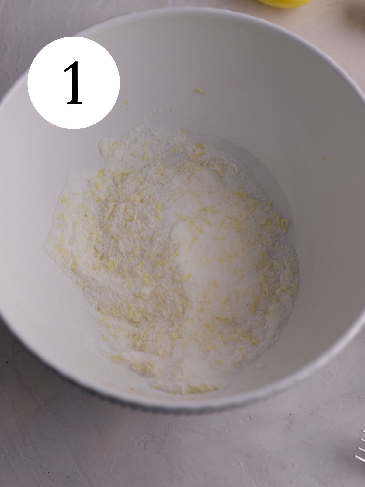 Sugar mixed together with lemon zest in a white mixing bowl. 