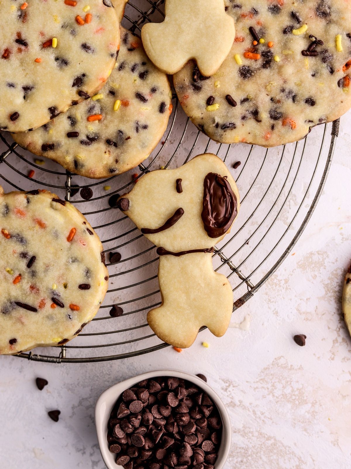 Pumpkin shaped cookies filled with sprinkles and chocolate chips and a snoopy cookie on a rack. 
