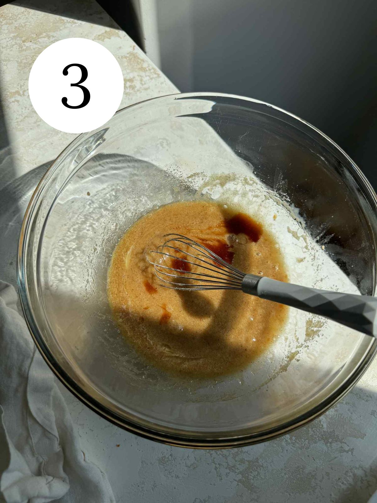 A glass mixing bowl with a whisk, vanilla and butter and sugar mixture.