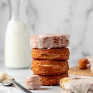 A stack of fried donuts and a glazed donut hole and a milk jug.