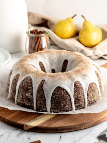 Chocolate bundt cake coated with cinnamon sugar and icing, two pears and some cinnamon sticks.